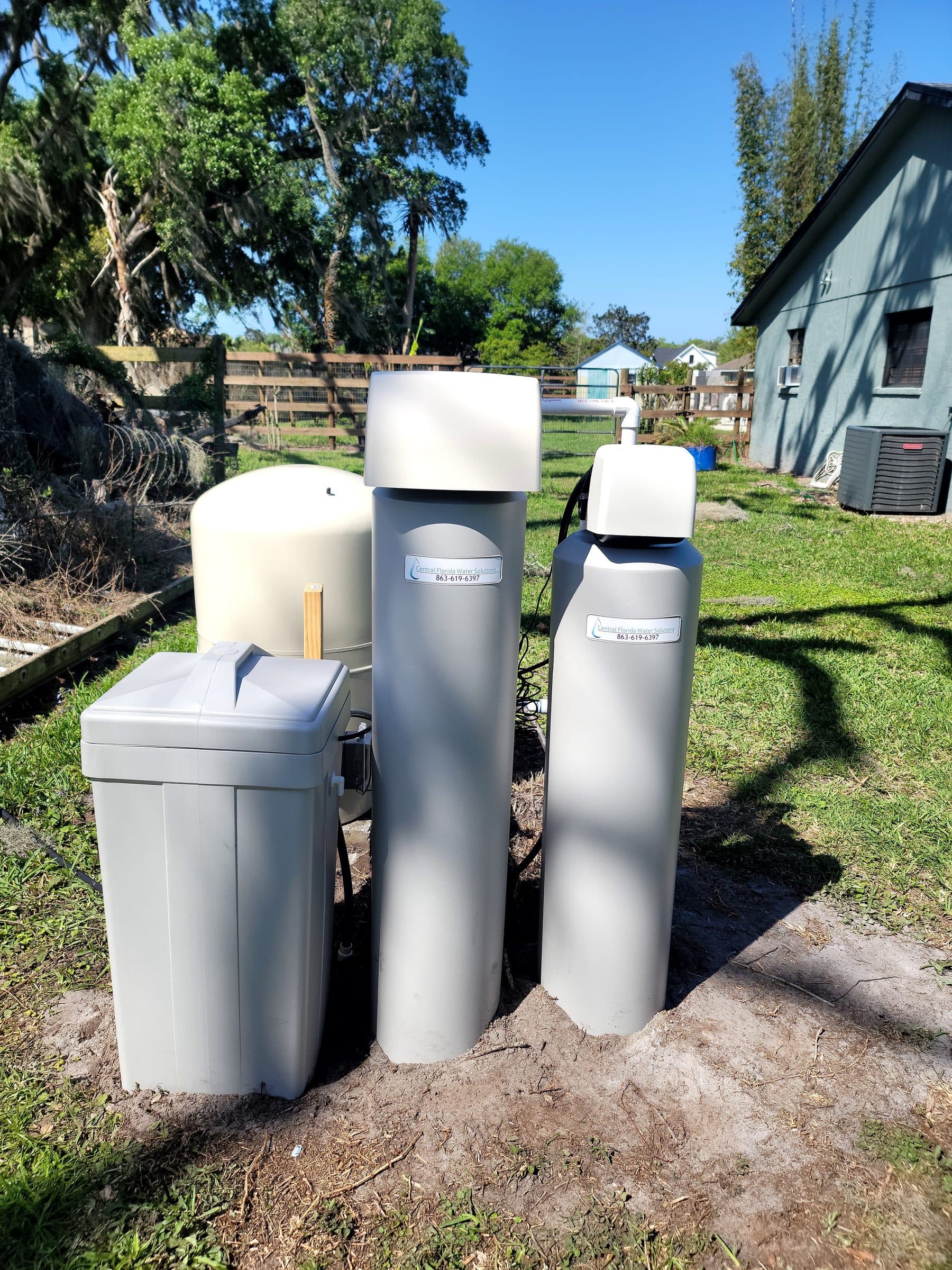 Twin softener tanks installed along a property fence line